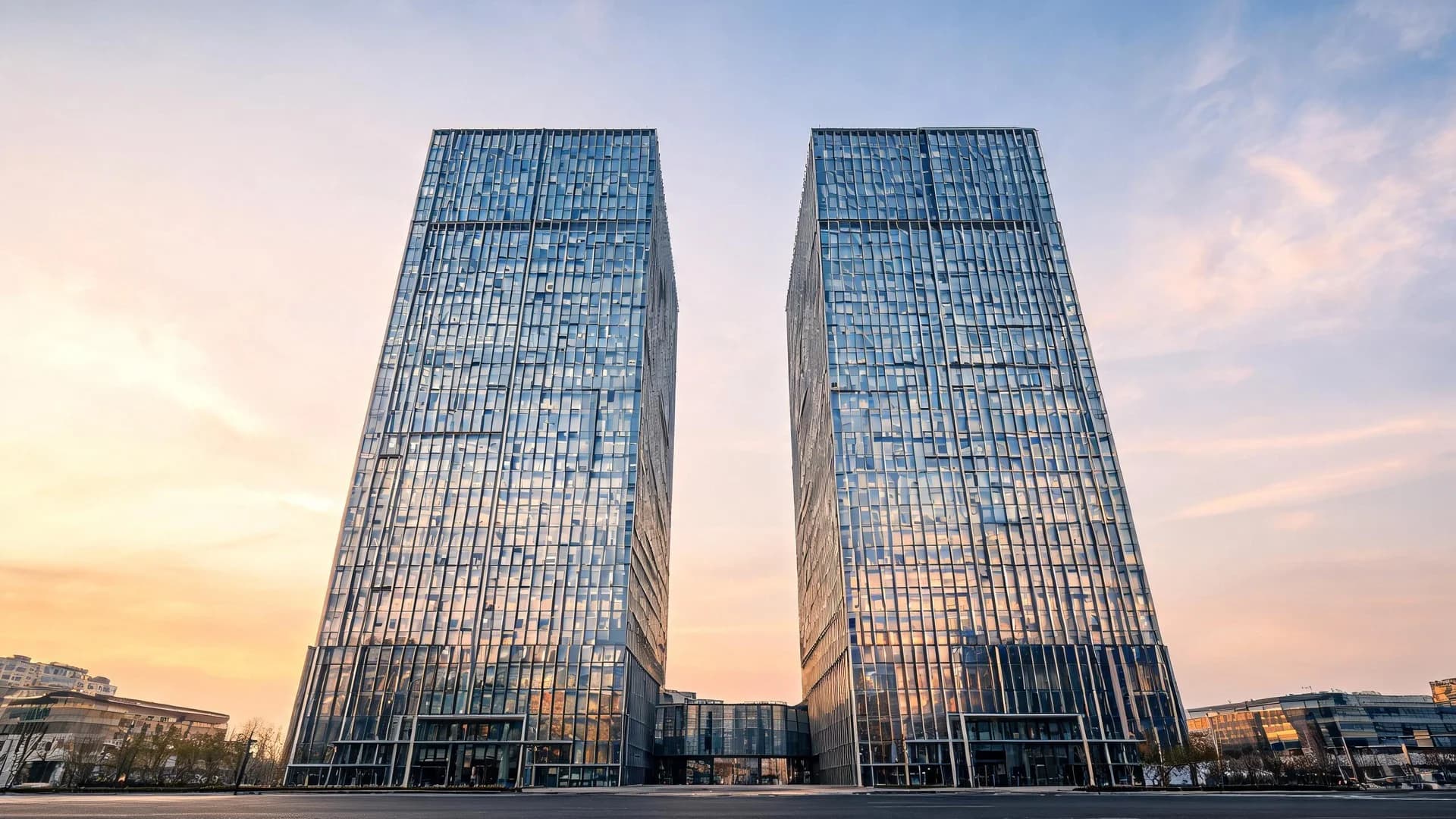 Two matching glass office towers standing side by side in a financial district, photographed from street level at golden hour.