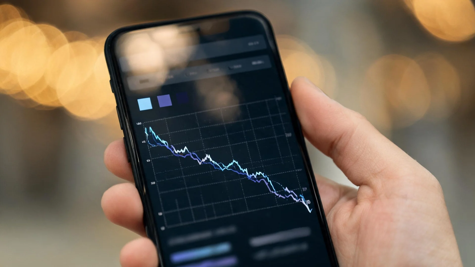A smartphone held in one hand showing an index comparison screen, with two fine tracking lines in light blue and indigo drawn across a gridded panel.